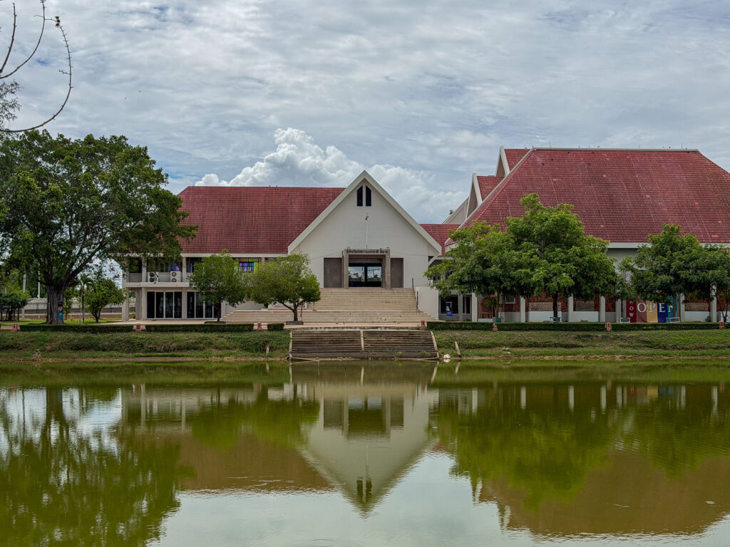 Fachada blanca del Museo Nacional de Phimai, con tejados rojos y su reflejo en un estanque