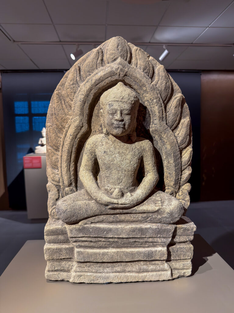 Pequeña escultura de Buda sentado, rodeada por un marco de piedra con formas onduladas