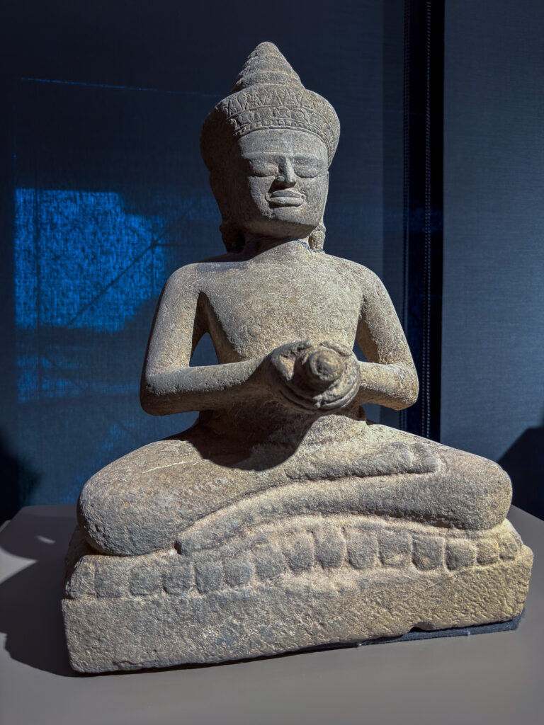 Figura de piedra sentada con las piernas cruzadas, tocado y un objeto entre las manos