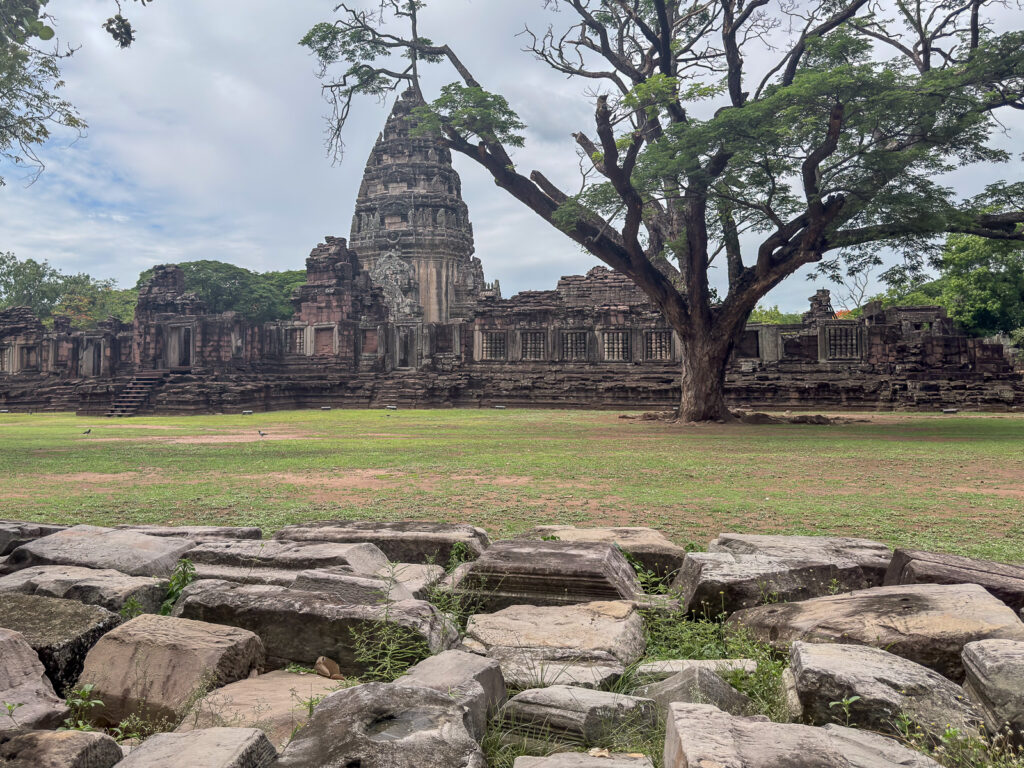 santuario, entre árboles y bloques de piedra. Templo de Phimai enmarcado por un árbol, con piedras en primer plano