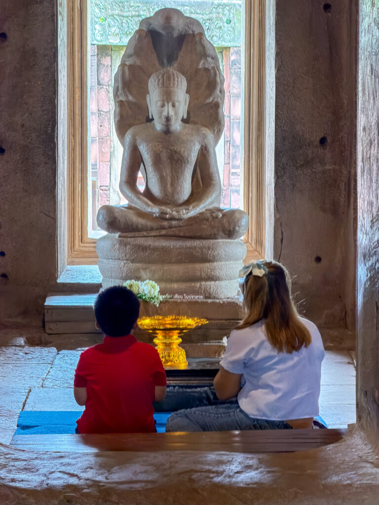 Dos visitantes sentados ante una imagen de Buda protegida por una naga en Phimai
